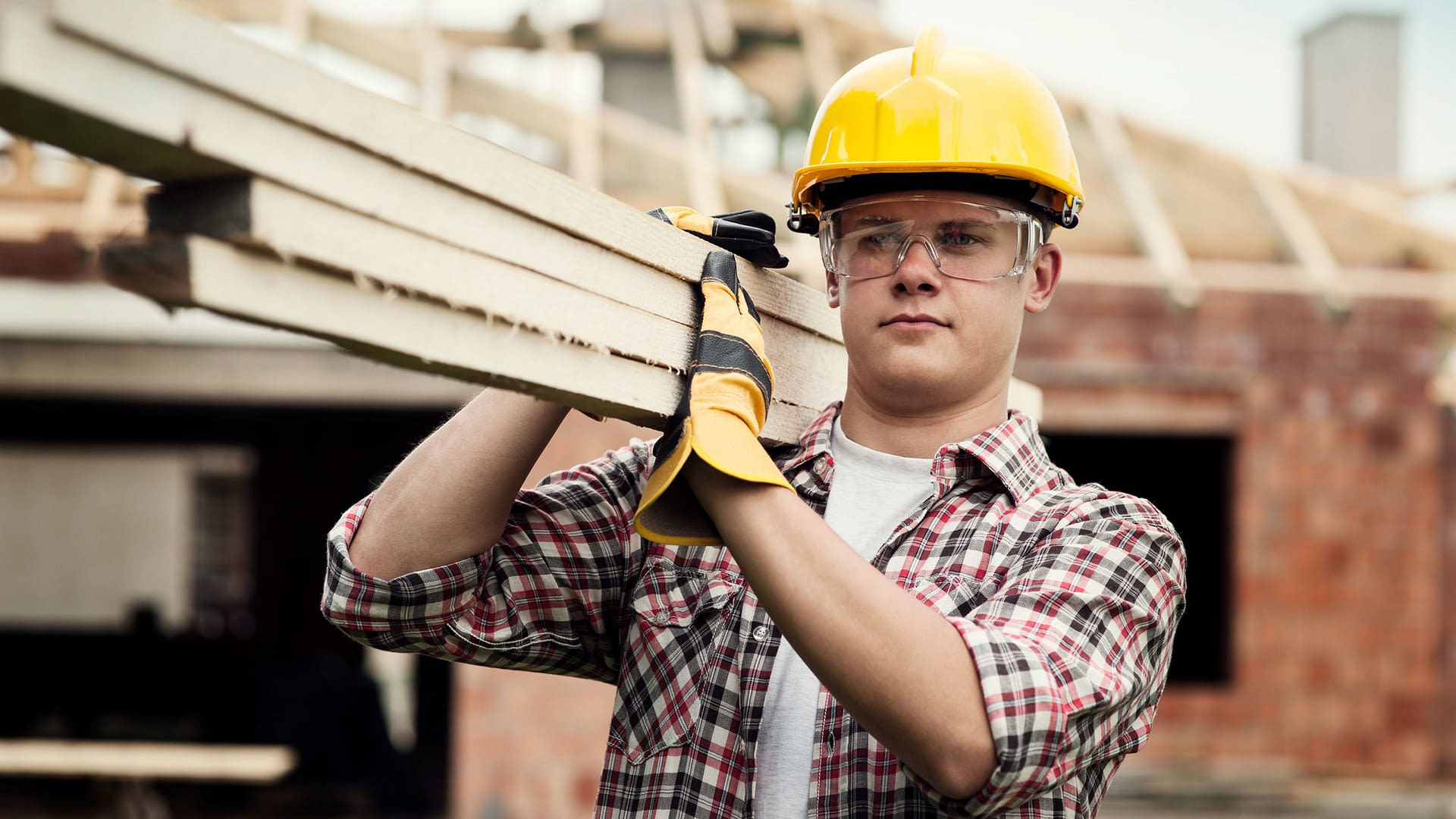 Construction worker carrying several boards on his shoulder.